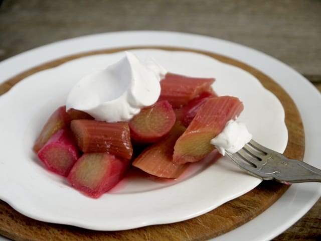  Poached Rhubarb with Vanilla Coconut  Cream  on a white plate with a fork on a wooden board