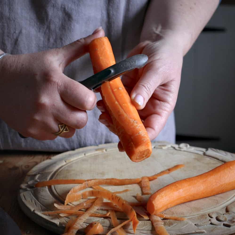 Woman peeling a carrot over a wooden chopping board 