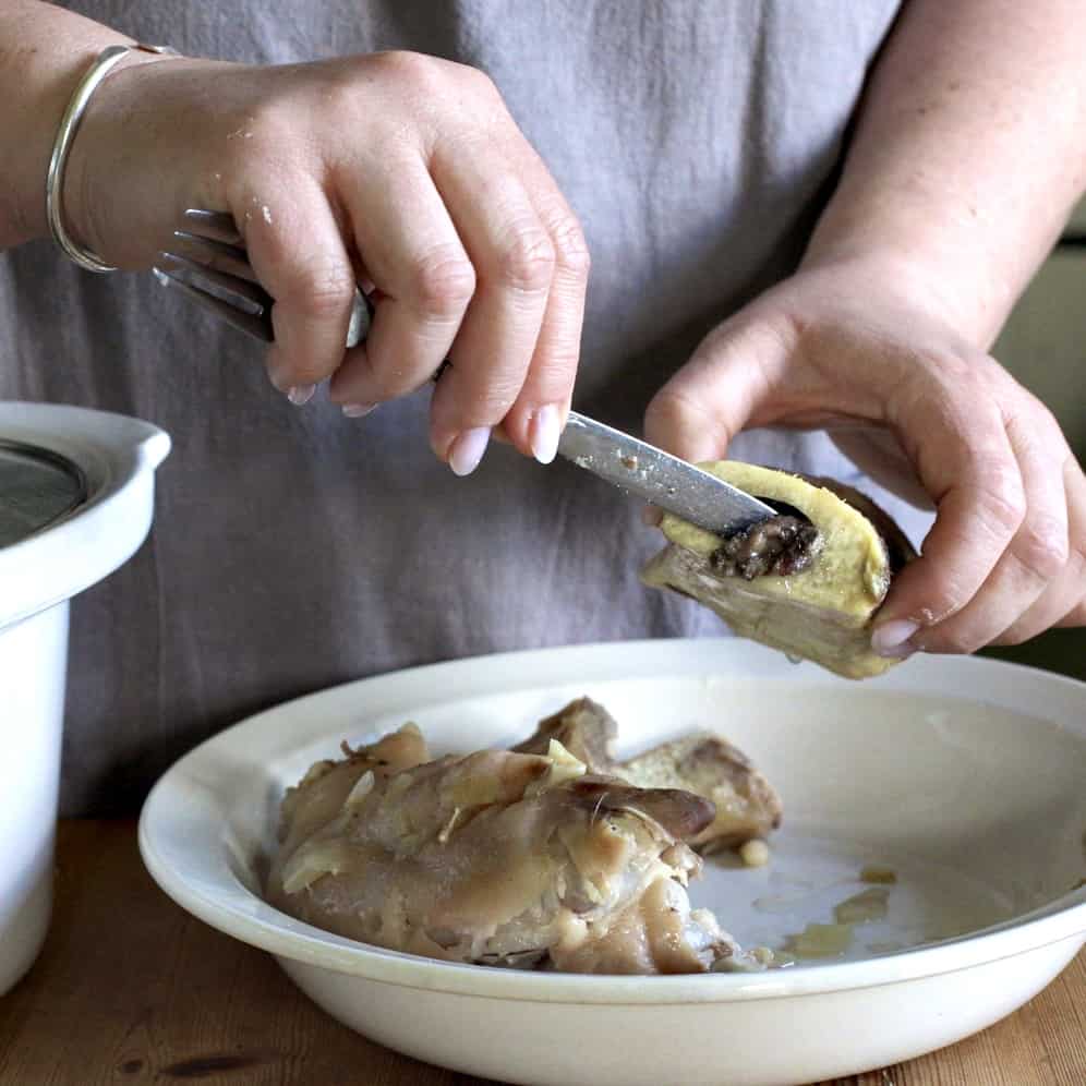 Woman scraping the marrow from a beef shin over a white bowl