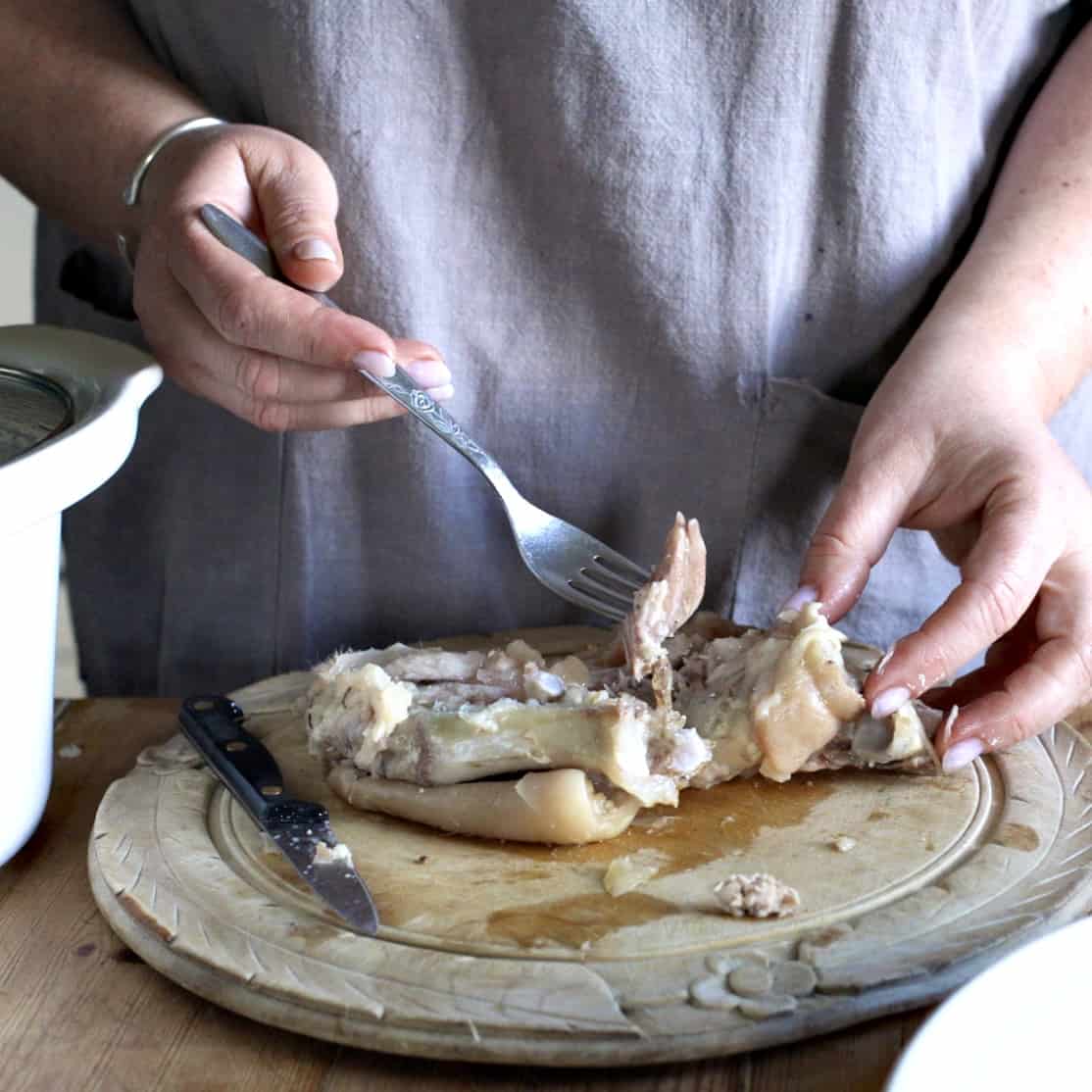 Woman removing the meat from inside a cooked pigs foot using a silver fork