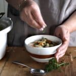 Woman sprinkling chopped parsley over a white bowl of bean and pork stew