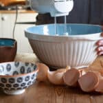 blue and white mixing bowl on a mess wooden kitchen counter with a white mixer mixing egg whites