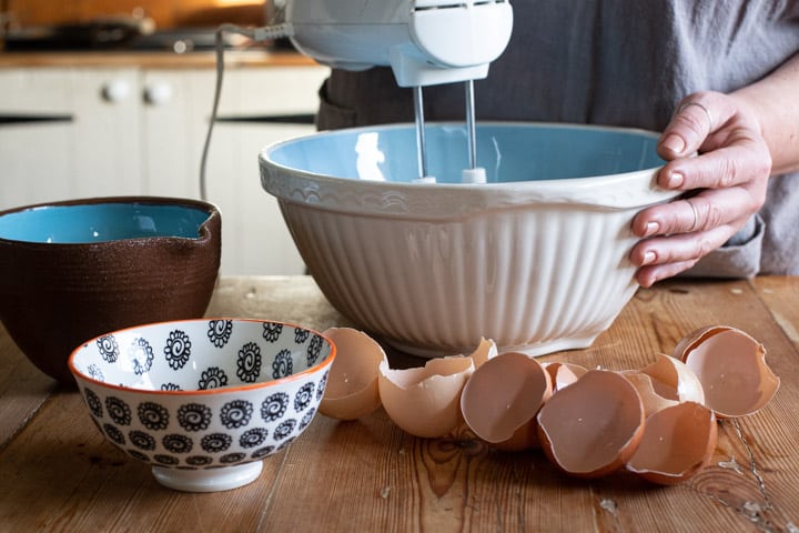 blue and white mixing bowl on a mess wooden kitchen counter with a white mixer mixing egg whites