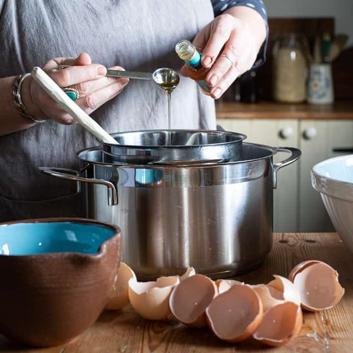 womans hands pouring vanilla essense from a small bottle into a silver bain marie into a silver saucepan 