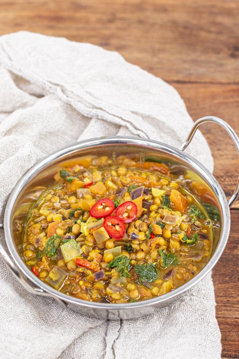 metal bowl of lentil and nettle curry on a wooden background