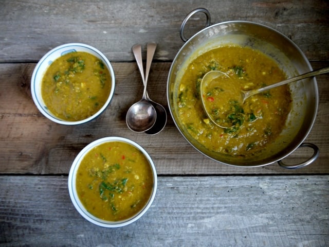 Lentil and Nettle Curry in a metal serving bowl and 2 white soup bowls with spoons on a wooden table