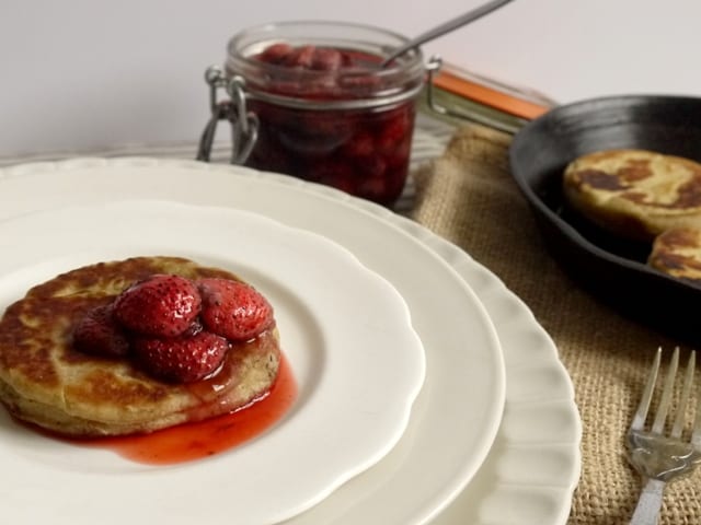Hot Griddle Cakes with Roast Strawberries on white plates beside a kilner jar of roast strawbwrries and a pan of griddle cakes
