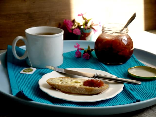 Breakfast tray with a slice of toaston a whiteplate with a knife , ajar of Rhubarb,Strawberry and Ginger Jam and a mug of tea