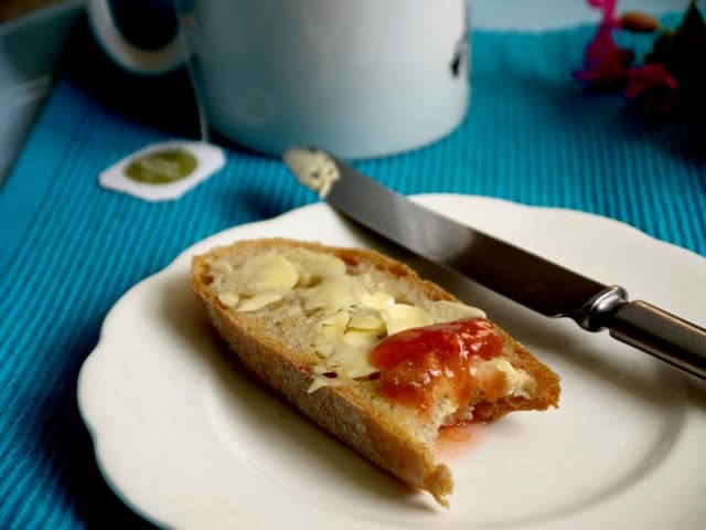 a slice of toast with Rhubarb,Strawberry and Ginger Jam on awhite plate with a butter knife