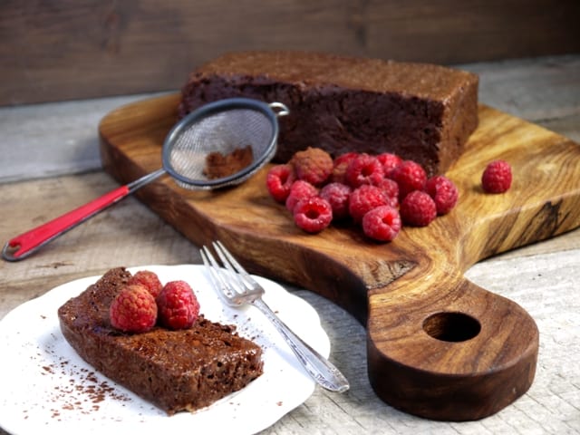 A wooden board with a French dessert called Chocolate Marquise and fresh raspberries on