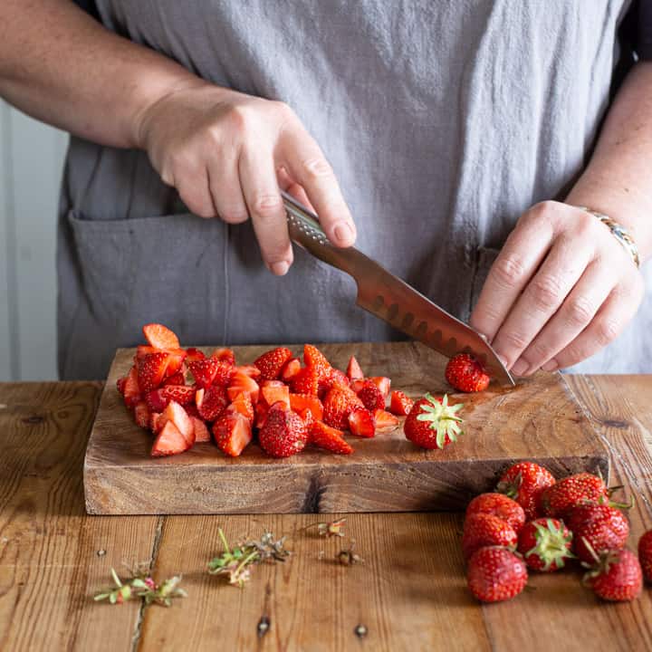 womans hands cutting up several strawberries on a wooden chopping board