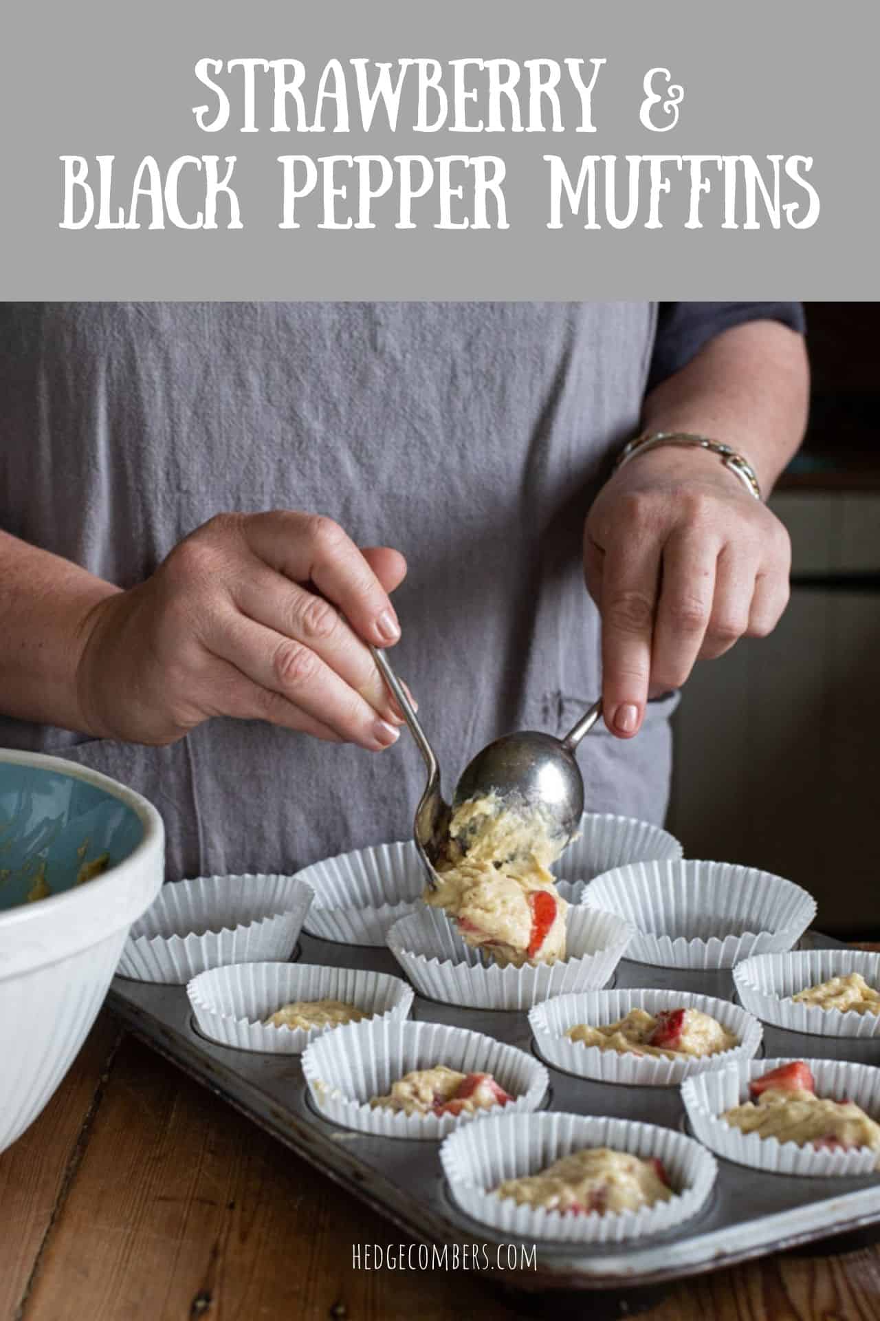 woman in grey scooping strawberry muffin batter from a blue mixing bowl into white paper muffin cases in a grey baking tin