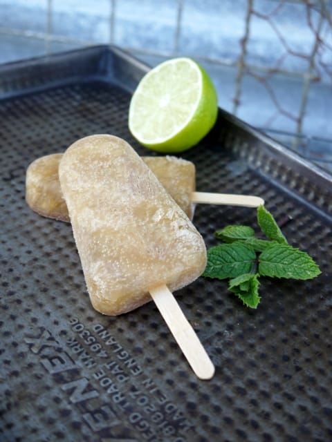  2 Froze Dark Rum Mojito Cocktail Lollies with half a lime and a sprig of mint on a black tray