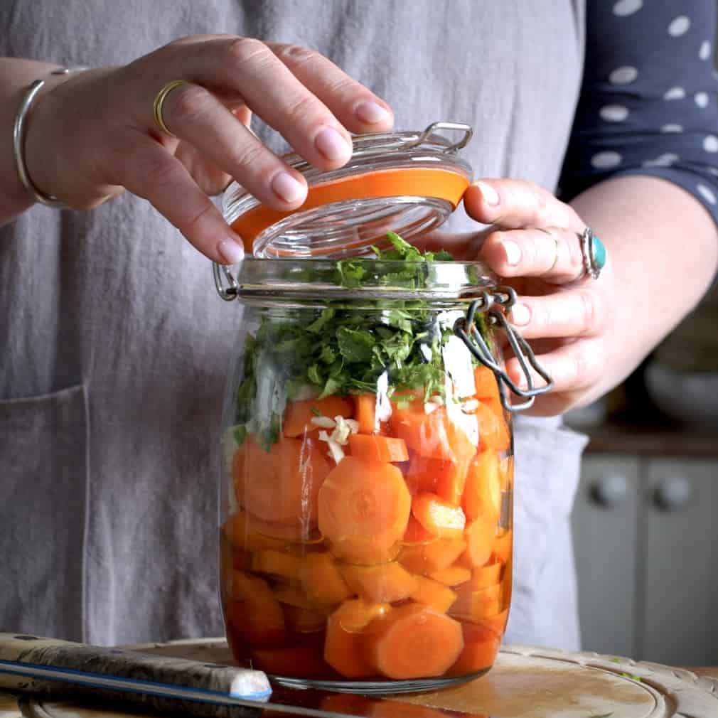 Woman closing the lid of a glass jar filled with carrots and coriander
