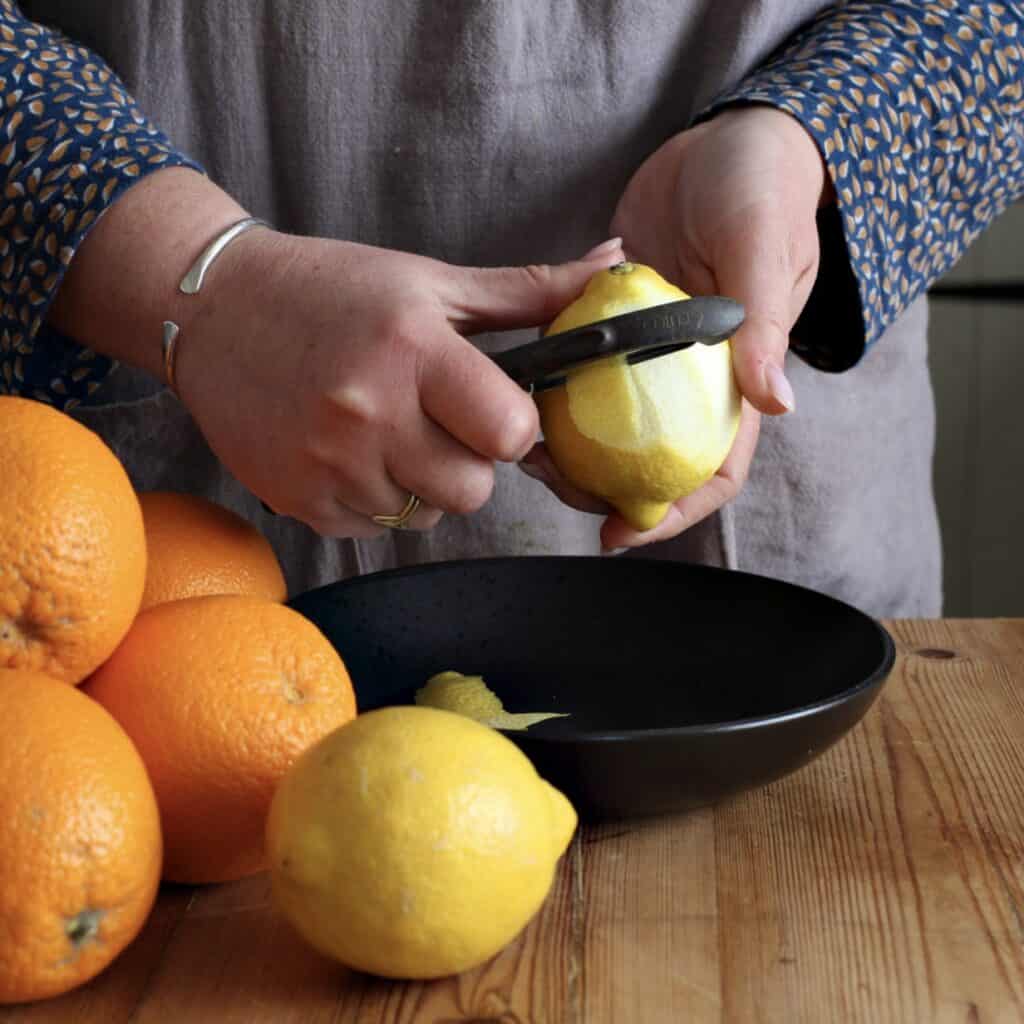 Woman in grey peeling a lemon with a black potato peeler