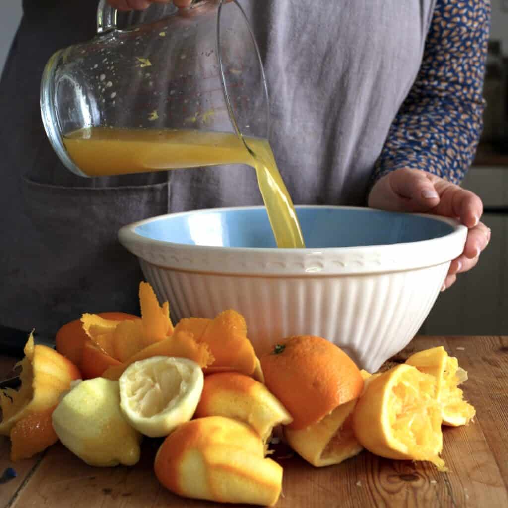 Woman in grey pouring an orange and lemon juice into a blue and white mixing bowl