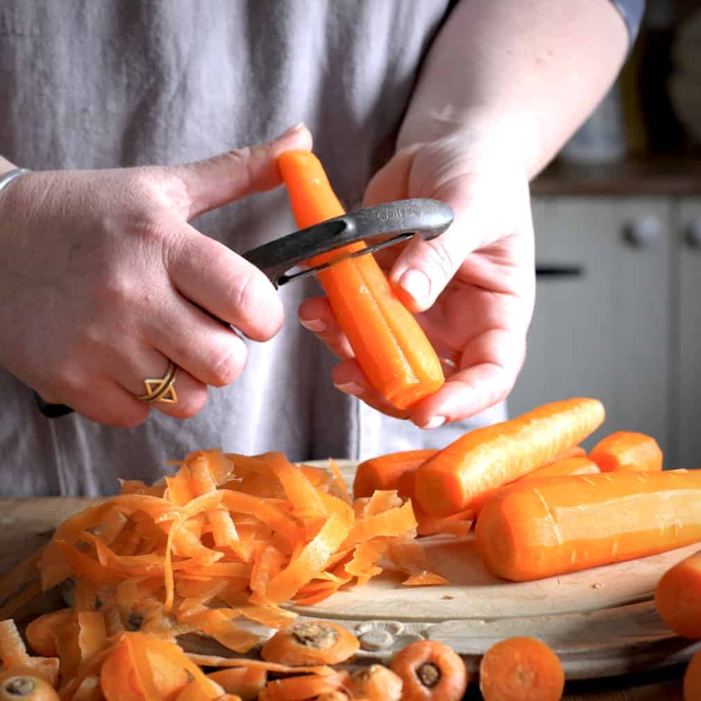 Woman in grey peeling carrots with a black potato peeler