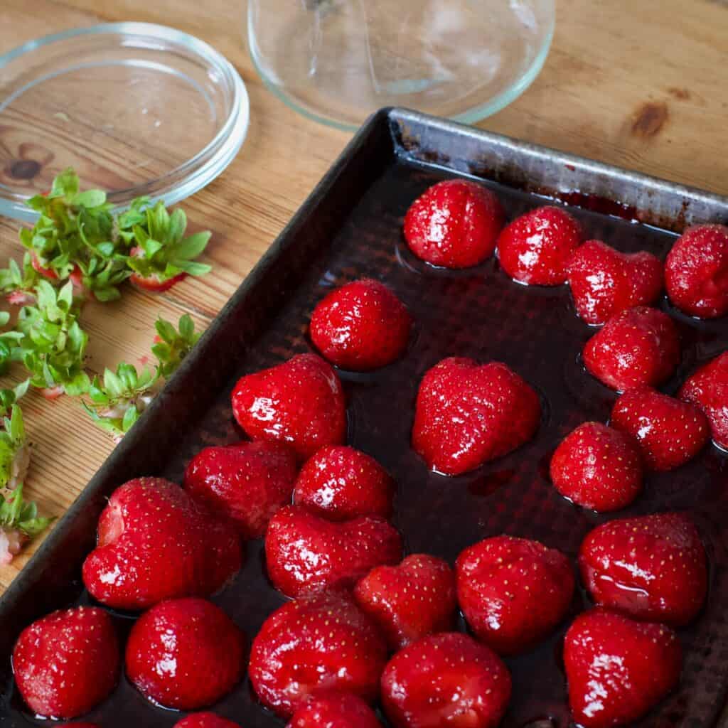 Black baking tray filled with juicy looking roast strawberries