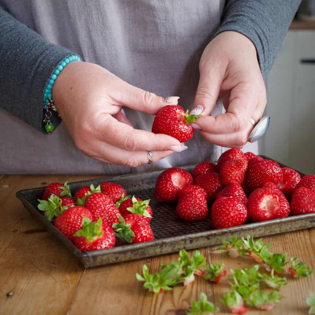 Womans hands removing the green leaves from a batch of strawberry’s before roasting