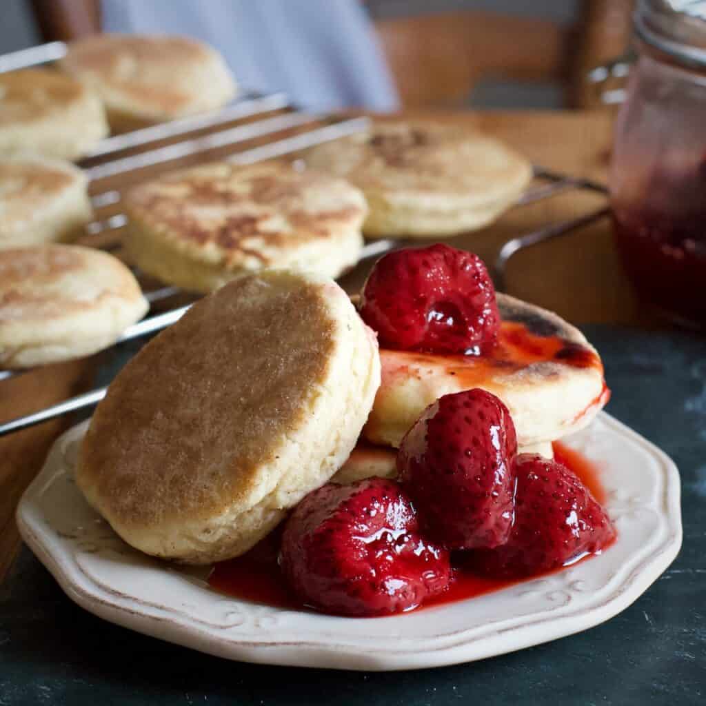 Bright red roast strawberries piled on top of 3 hot griddle cakes on a small white plate