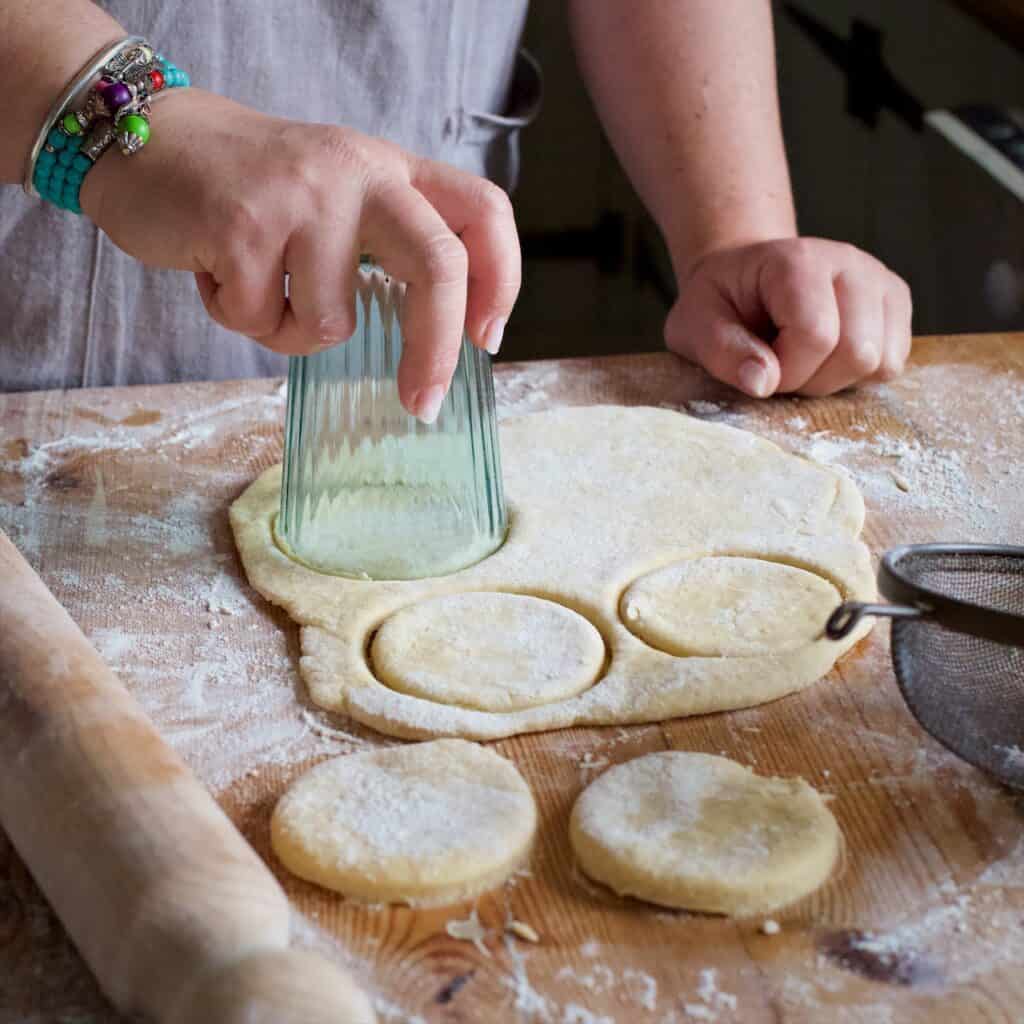 Womans hands cutting out disks of griddle cake dough with an upturned glass as a cutter
