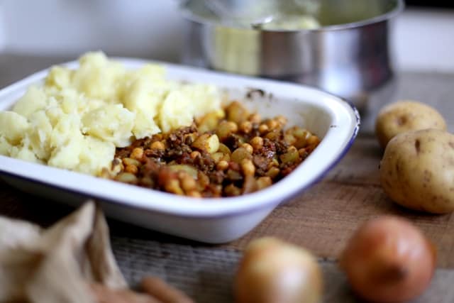 moroccan Shepherd's Pie in an enamel dish on a table surrounded by vegetables and cookware