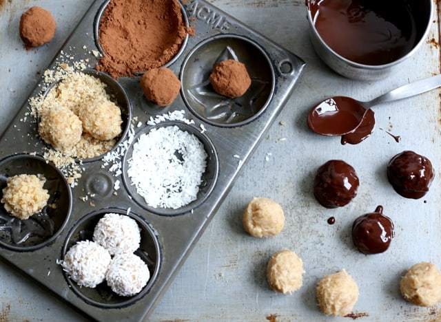 messy baking shot with handmade cookie dough truffles on a metal baking sheet with melted dark chocolate 