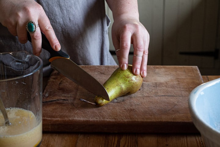 womans hands cutting up a green pear on a wooden chopping board