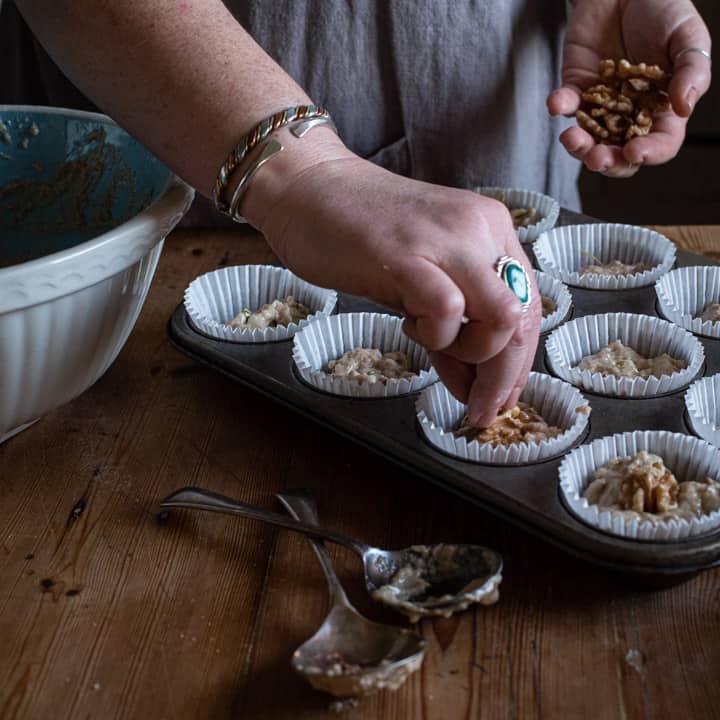 womans hands placing a wlnut half on top on a tray of muffins