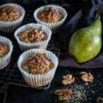 black background and 5 pear muffins on a rustic cooling rack with raw green pears and walnut halves scattered around