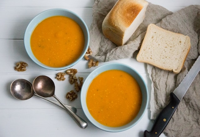 Sweet Potato, Walnut and Sage Soup with soup spoons ,bread and scattered walnuts on a white cloth