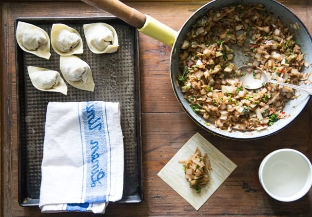 Wontons made using vegetarian wontons recipe on a tray beside a kitchen cloth with saucepan of filling and a tray of wonton waiting to br rolled