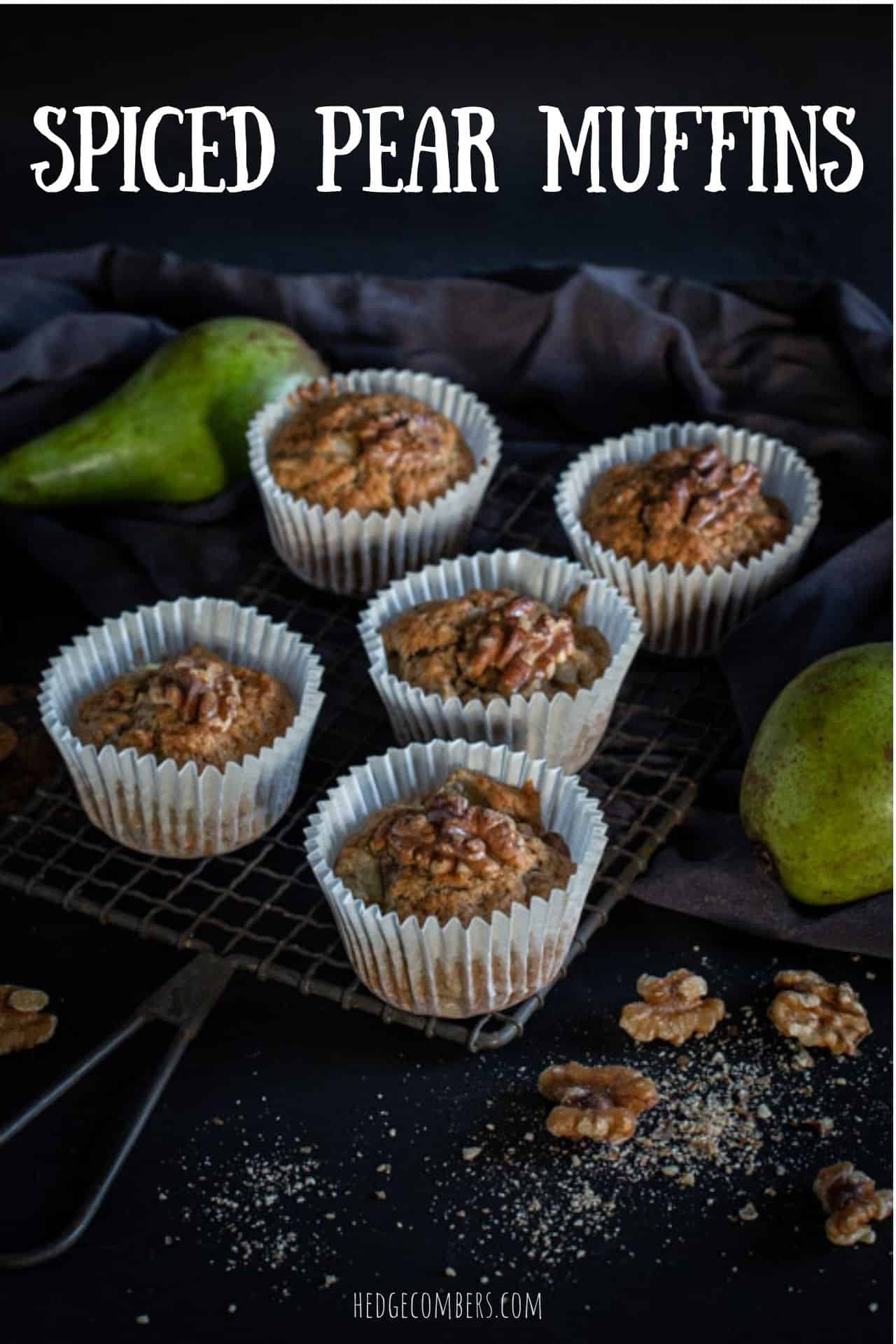 black background and 5 pear muffins on a rustic cooling rack with raw green pears and walnut halves scattered around