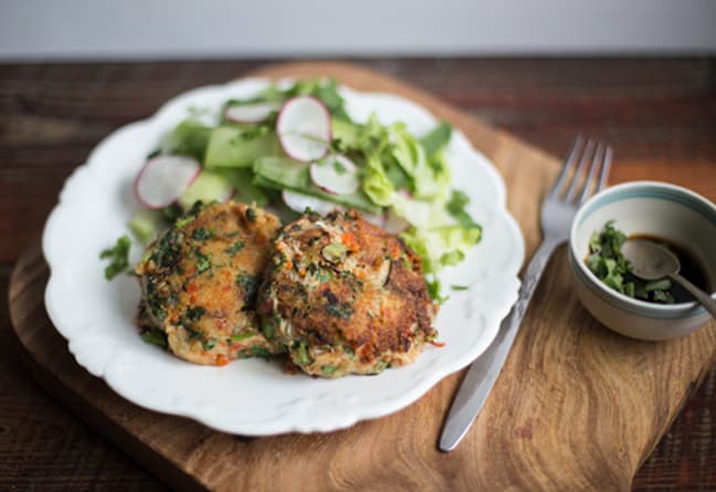 wooden chopping board with white plate holding crab cakes and green salad