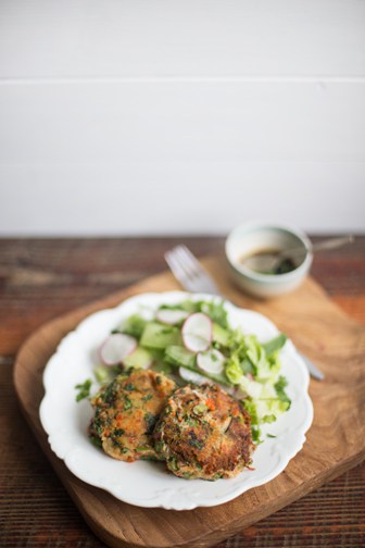 wooden chopping board with white plate holding crab cakes and green salad