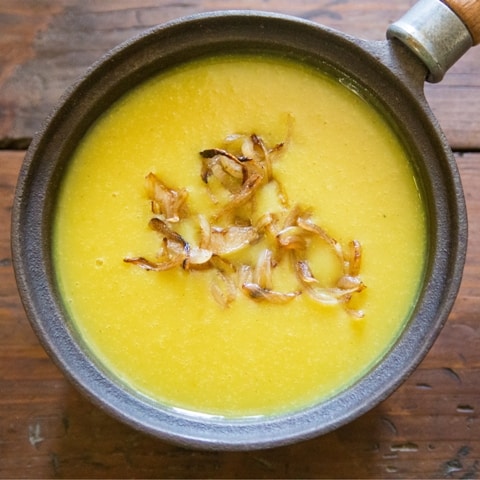 bright yellow creamy soup in a black pan topped with fried onions