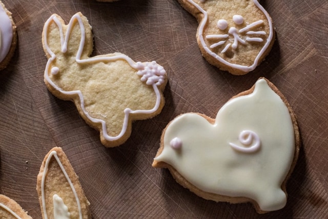  Dairy Free Easter cookies in the shape of rabbits, eggs and chicks, laid out on a wooden board