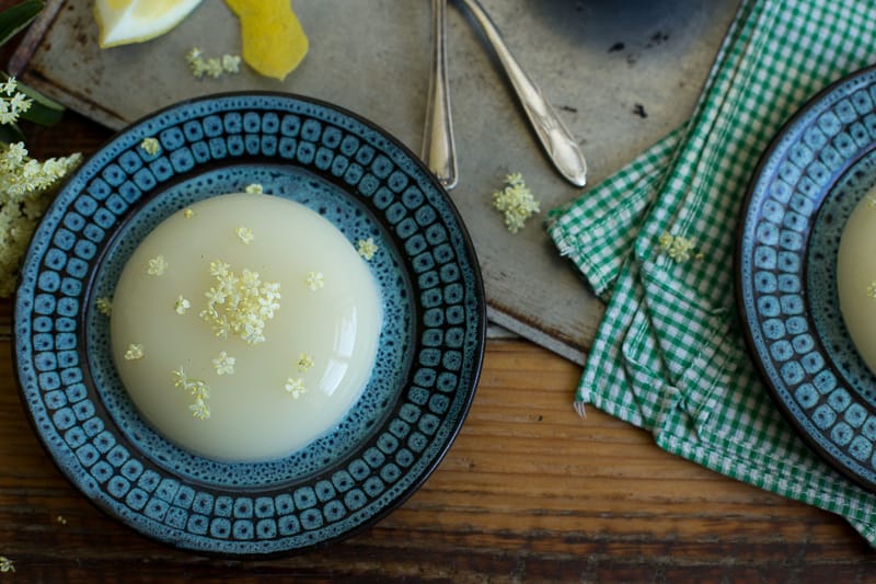  2 Elderflower Panna Cotta (Deliciously Dairy Free!) on blue plates on a kitchen table with spoons and elderflowers