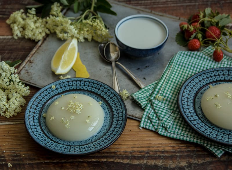  2 Elderflower Panna Cotta (Deliciously Dairy Free!) on blue plates on a kitchen table with spoons and elderflowers 
