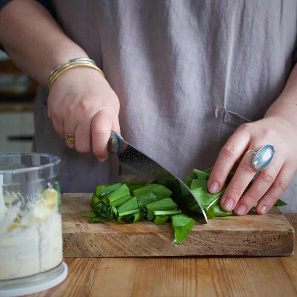 Womans hands chopping fresh wild garlic leaves on a wooden chopping board 