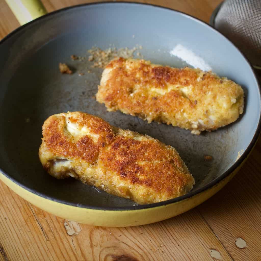 Small frying pan on a wooden kitchen counter containing two golden brown chicken Kiev 