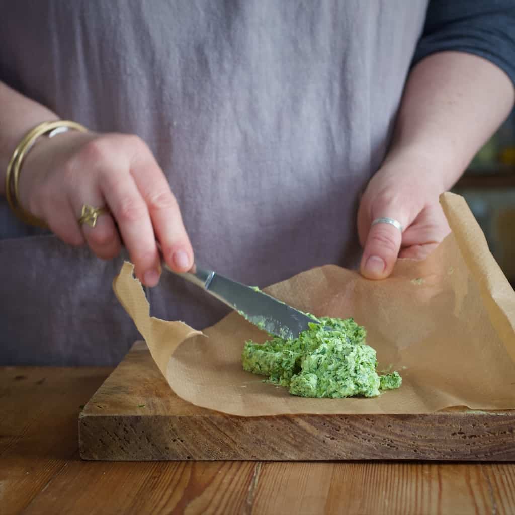 Womans hand placing green wild garlic butter onto a brown piece of baking paper
