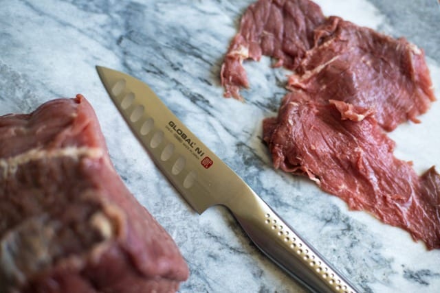 Thinly sliced beef for jerky with a knife on a marble board