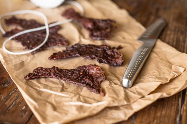 Salt and Pepper Beef Jerky using jerky on brown paper with string and a fluted cooks knife