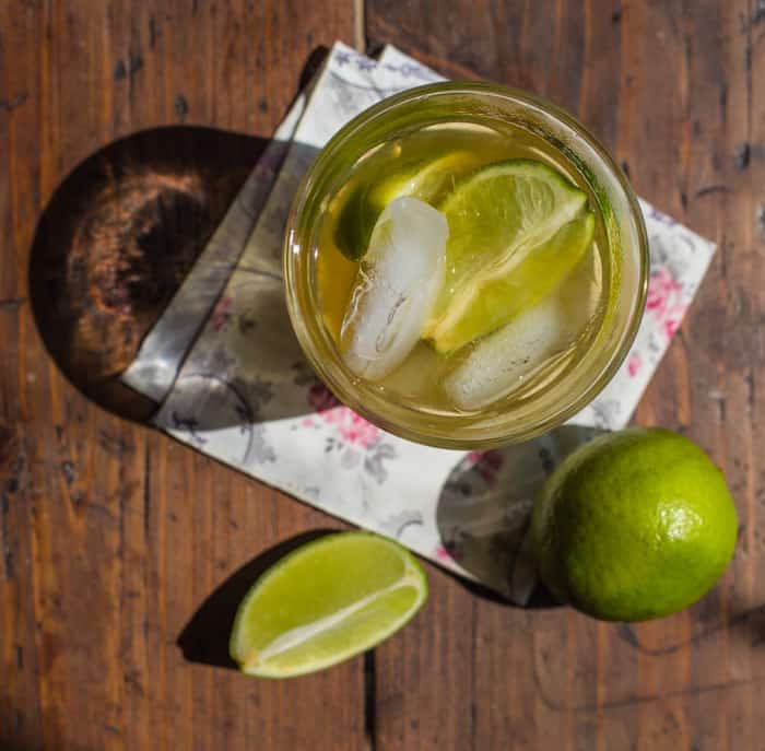 A glass of caipirinha cocktail recipe beside limes on an outdoor table from above