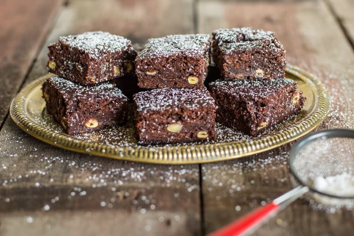 6 Green Hazelnut Brownies piled on a plate on a wooden table with a small sieve of icing sugar