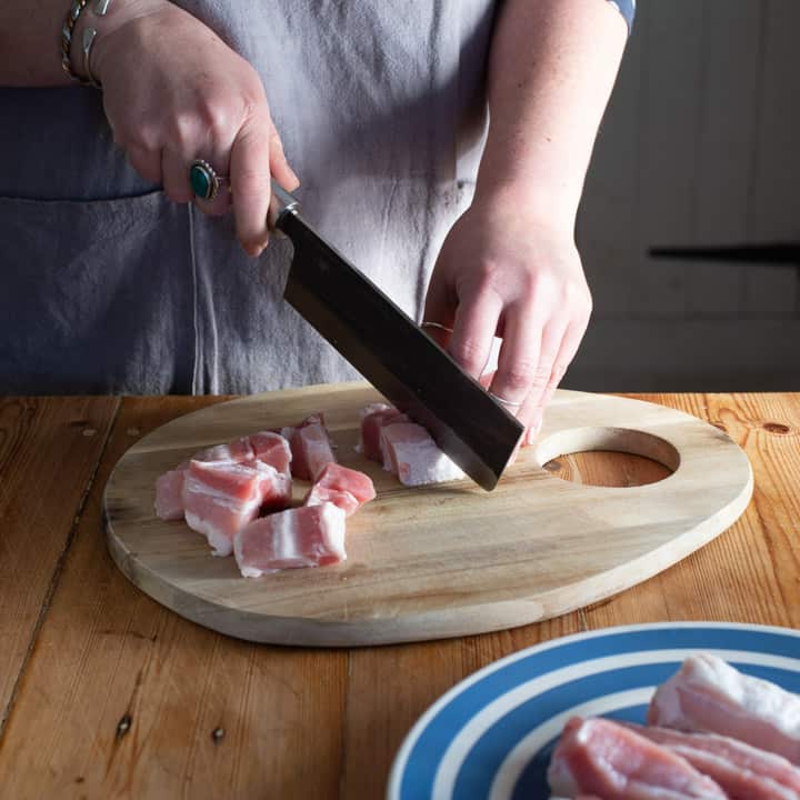 womans hands dicing pork belly in rustic kitchen