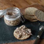 wooden board with glass jar of rabbit terrine, oat cakes and a small silver knife