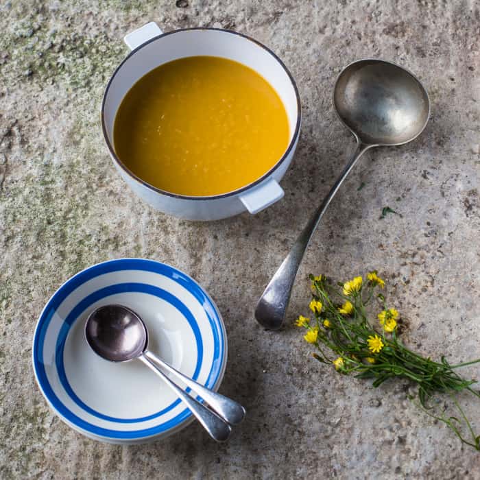 Leek and Sweet Potato Soup in an large pot with a ladle ,soup bowl and spoon on a snowy backdrop