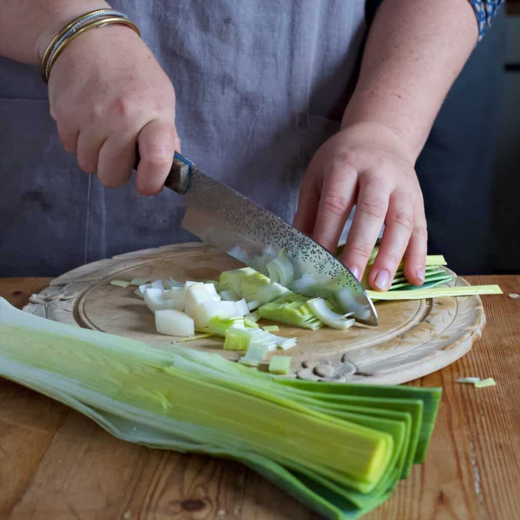 Womans hands chopping leeks on a rustic wooden chopping board